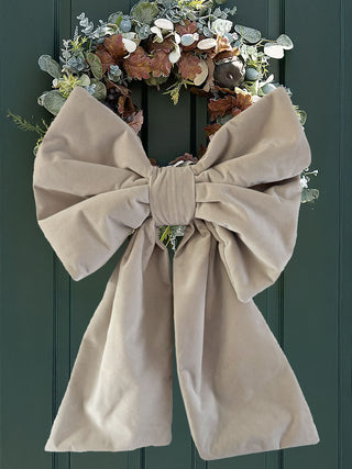 Decorative wreath with a large beige bow on a green door