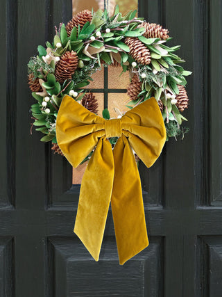 Wreath with greenery, pinecones, and a yellow bow on a dark surface