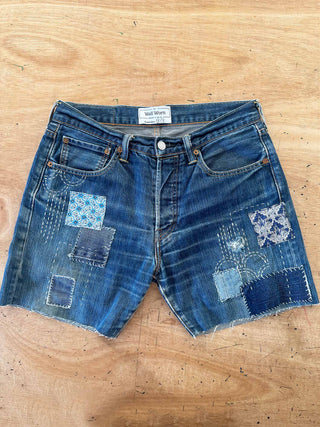 Pair of blue denim shorts with patchwork design on a wooden surface