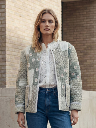 Woman wearing a floral quilted jacket in front of a brick wall.