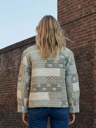 Person wearing a patterned jacket standing against a brick wall.
