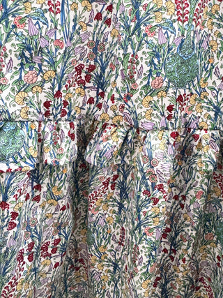 A close-up of a tiered dress or skirt featuring an all-over dense floral and botanical print on a light cream background. The pattern includes blue, green, red, pink, and yellow wildflower-like motifs.