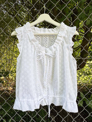 White lace top on a hanger against a chain-link fence and greenery background