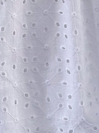Close-up of a white eyelet fabric with a geometric embroidered pattern and small cutout details.