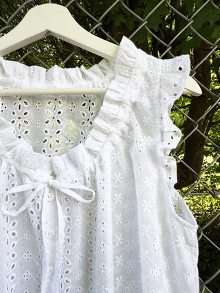 White lace top on a hanger against a chain-link fence and greenery background