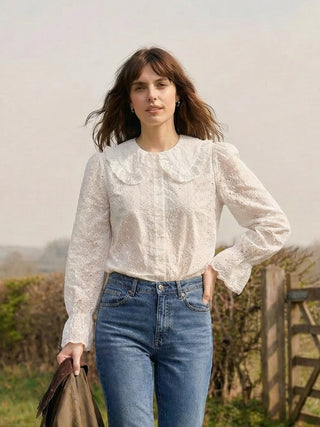 Woman wearing a white blouse and blue jeans standing outdoors with a blurred background