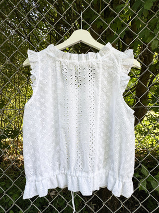 White lace top on a hanger against a chain-link fence and greenery background