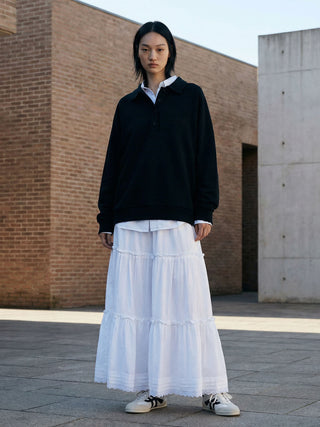 Person wearing a black sweater and white skirt standing in front of a modern architectural building.